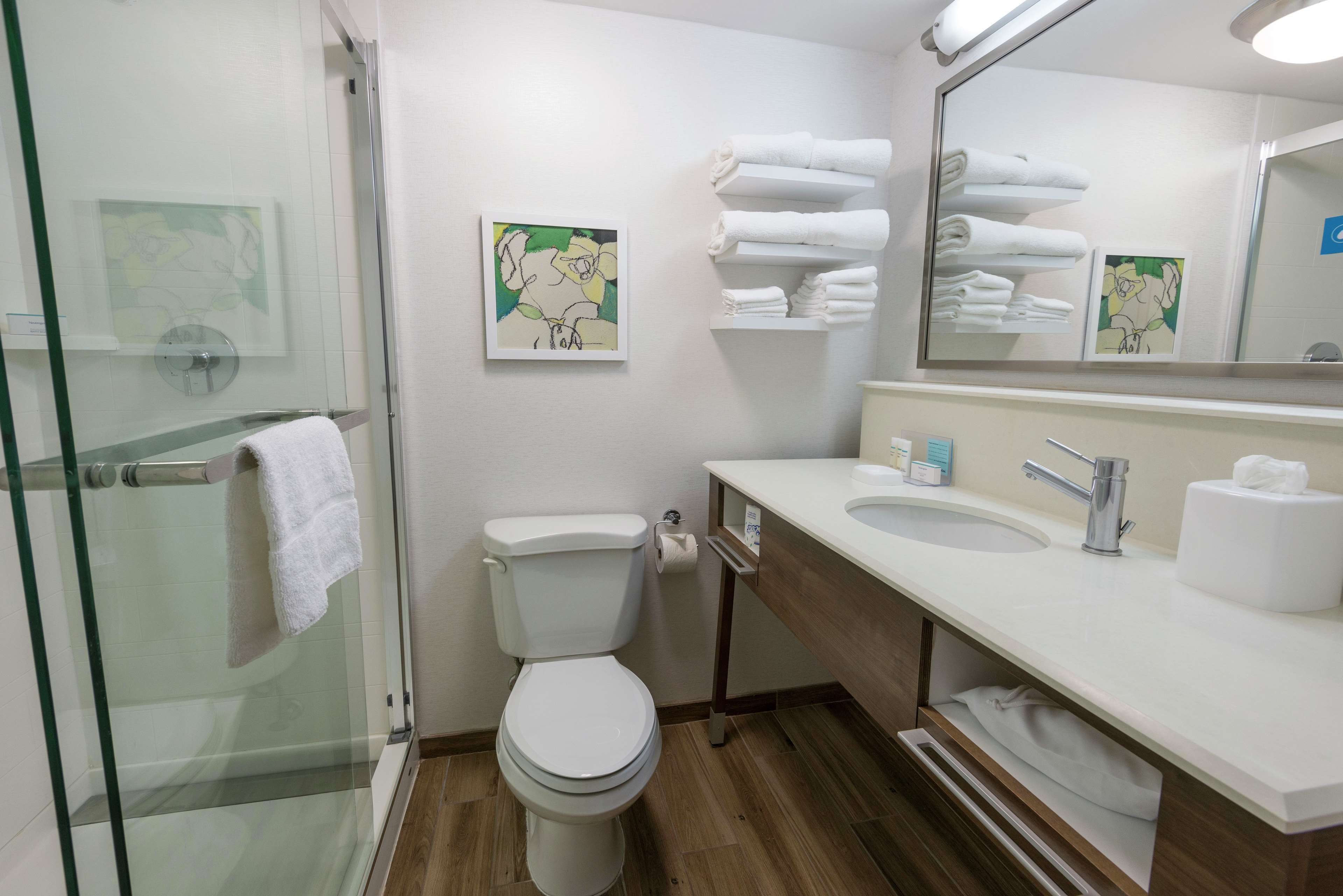 Un baño moderno con cabina de ducha de vidrio, inodoro, lavabo con espejo y toallas ordenadas.