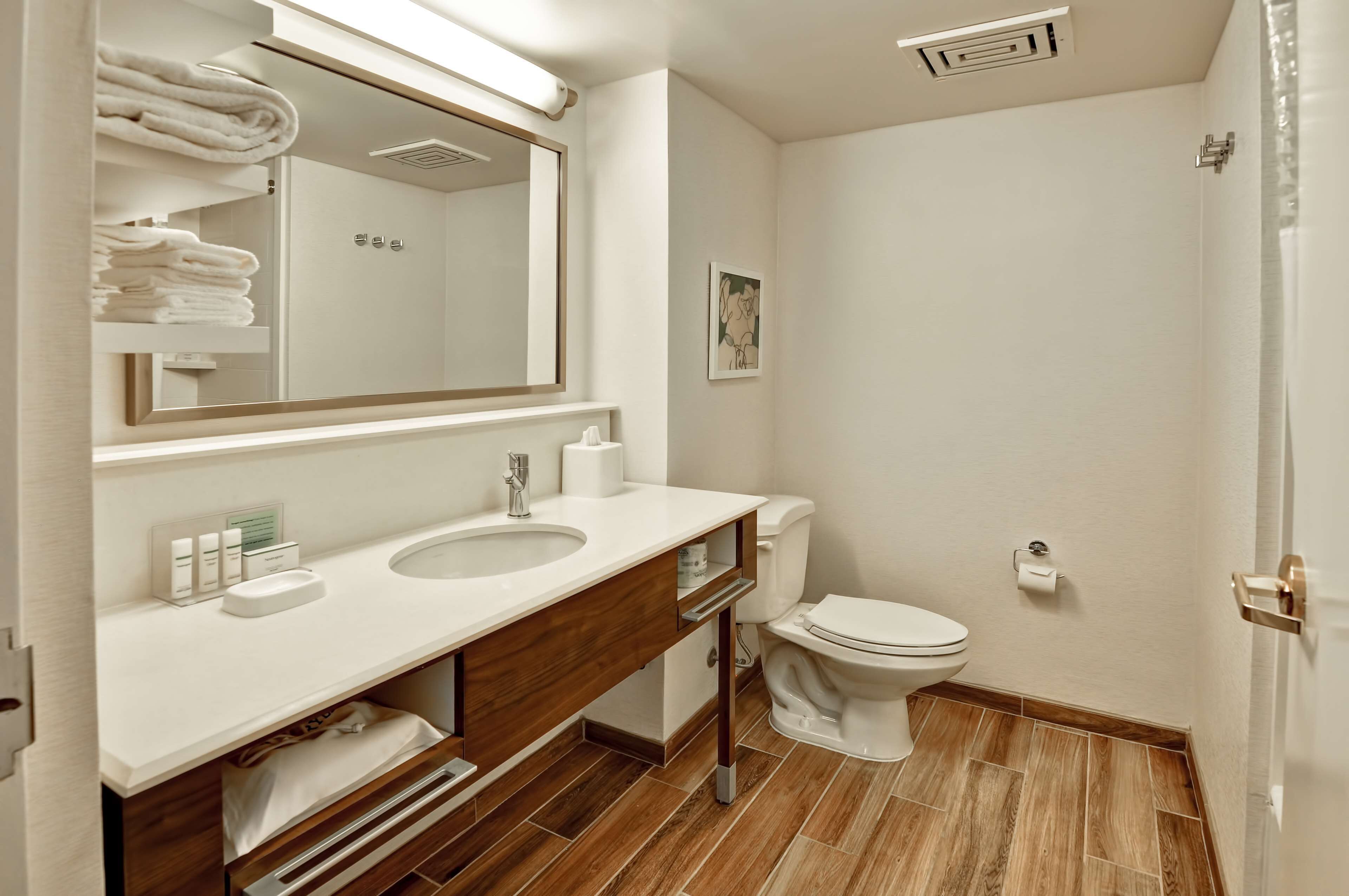 Une salle de bain moderne avec un grand miroir, deux lavabos, des toilettes et un revêtement de sol en bois.