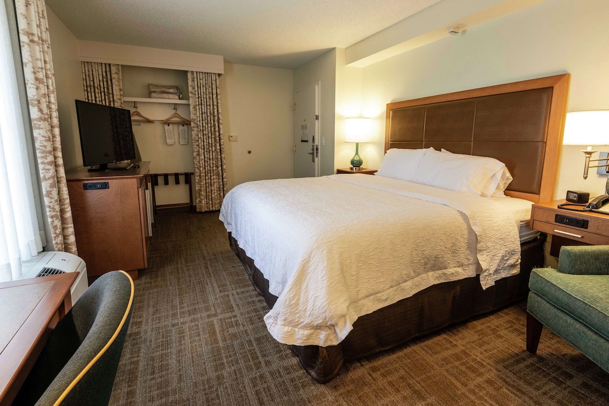 A hotel room with a large bed, a desk with a chair, a television, and a lamp.