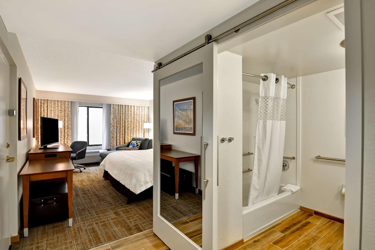 A hotel room with a bed, desk, chair, and a shower area.