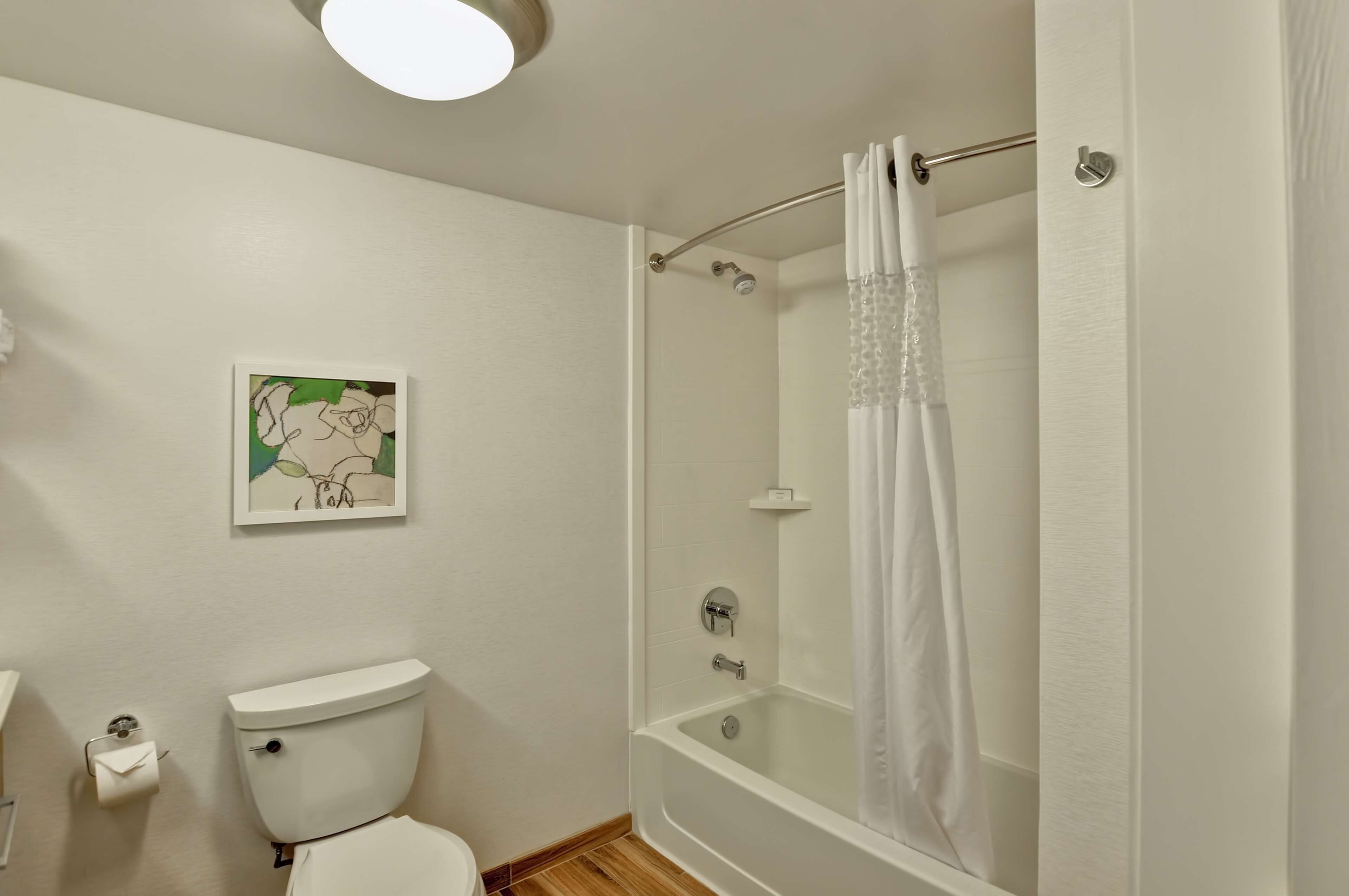 A bathroom with a toilet, a shower with a glass door, and a wall-mounted picture.