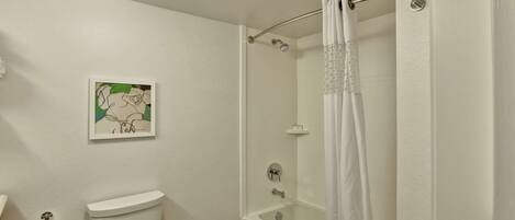 A bathroom with a toilet, a shower with a glass door, and a wall-mounted picture.