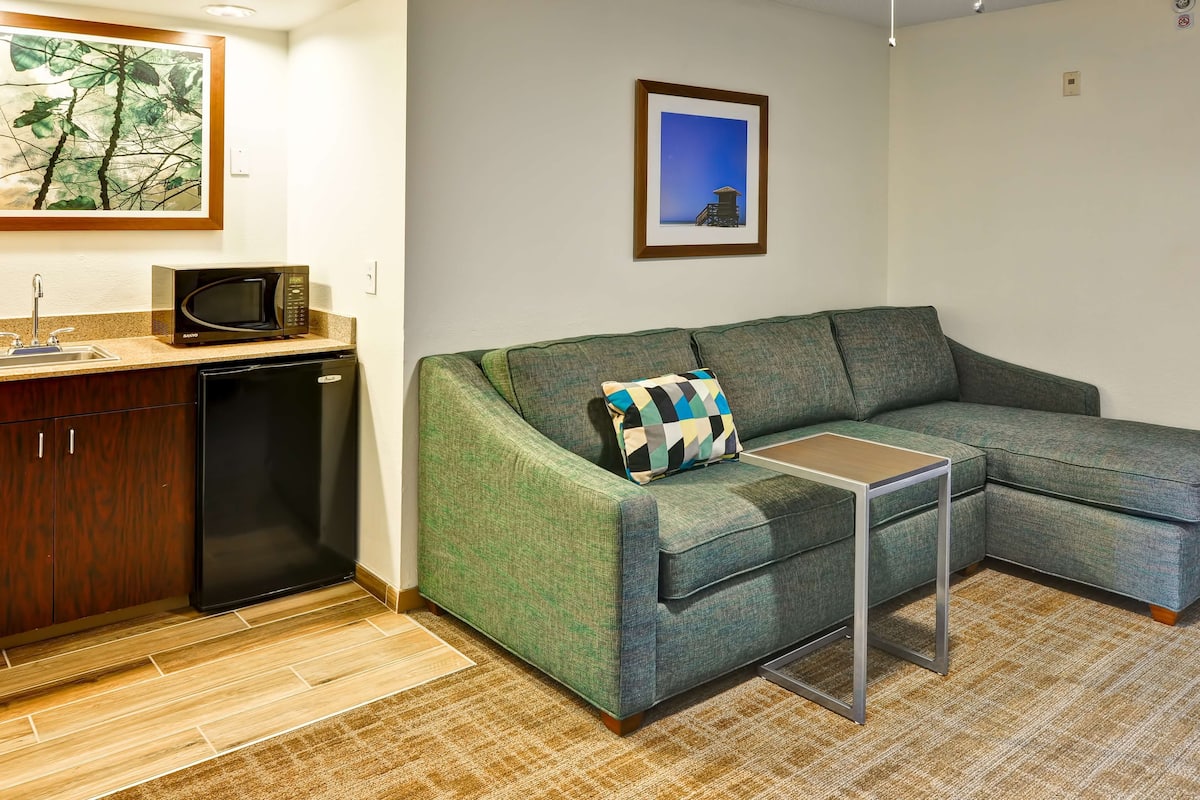 A compact living space with a green sofa, a small table, a microwave, and a dishwasher.
