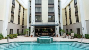 Et moderne hotel med en central gårdhave, hvor der er swimmingpool, udendørs siddepladser og krukker med planter.