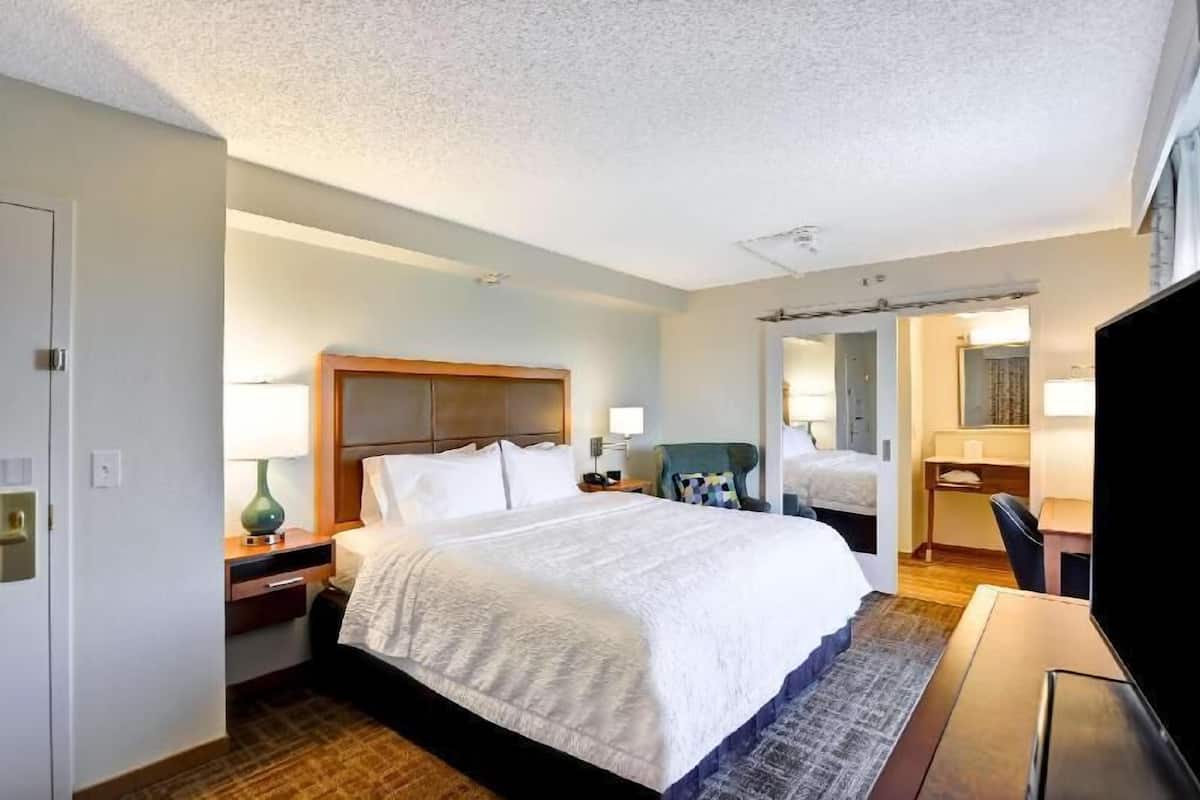A hotel room with a large bed, a desk with a chair, a television, and a bathroom visible through an open door.