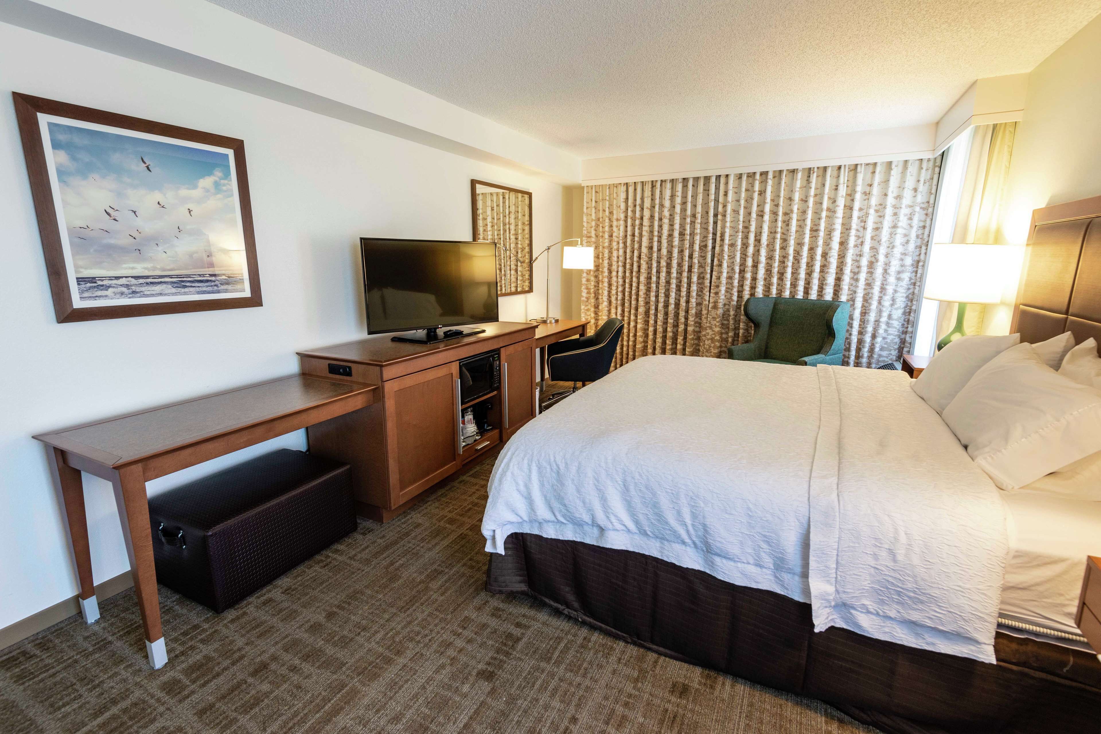 A hotel room with a bed, desk, television, and a window with curtains.