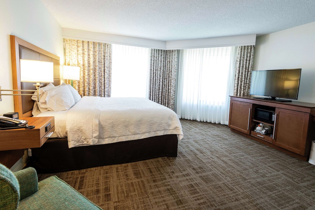 A hotel room with a bed, a desk with a telephone, a television on a cabinet, and a window with curtains.