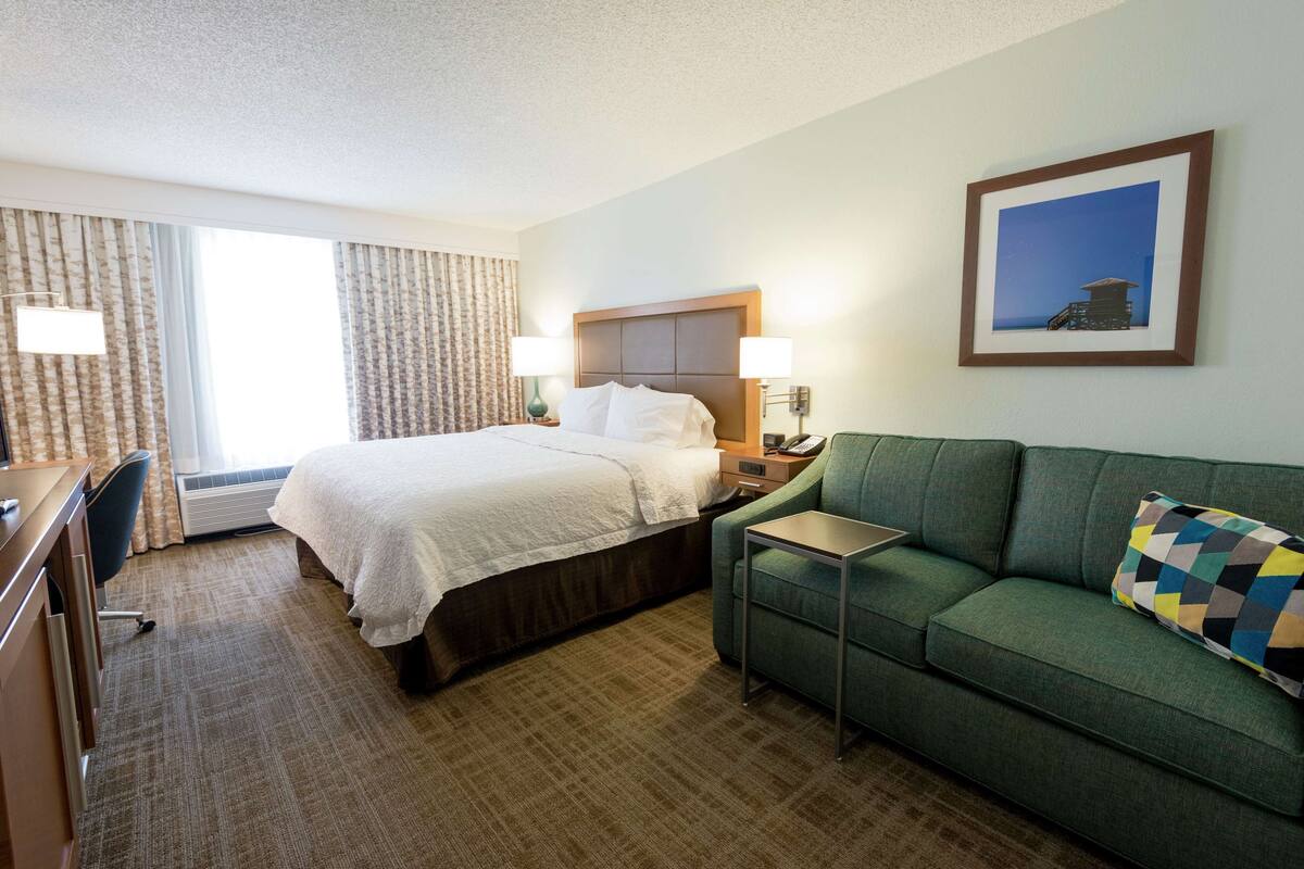 A hotel room with a bed, a green sofa, a desk, and a framed picture on the wall.