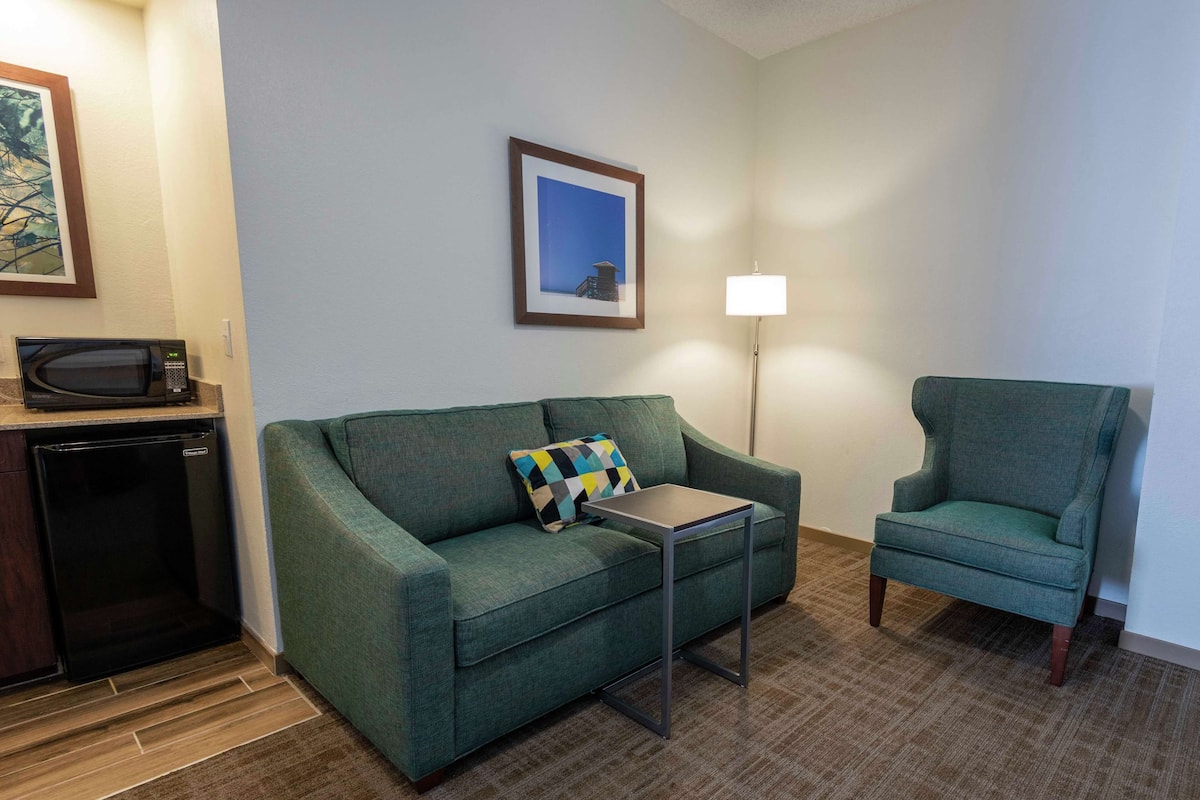 A compact living space with a green sofa, a matching armchair, a small table, a microwave, and a refrigerator.