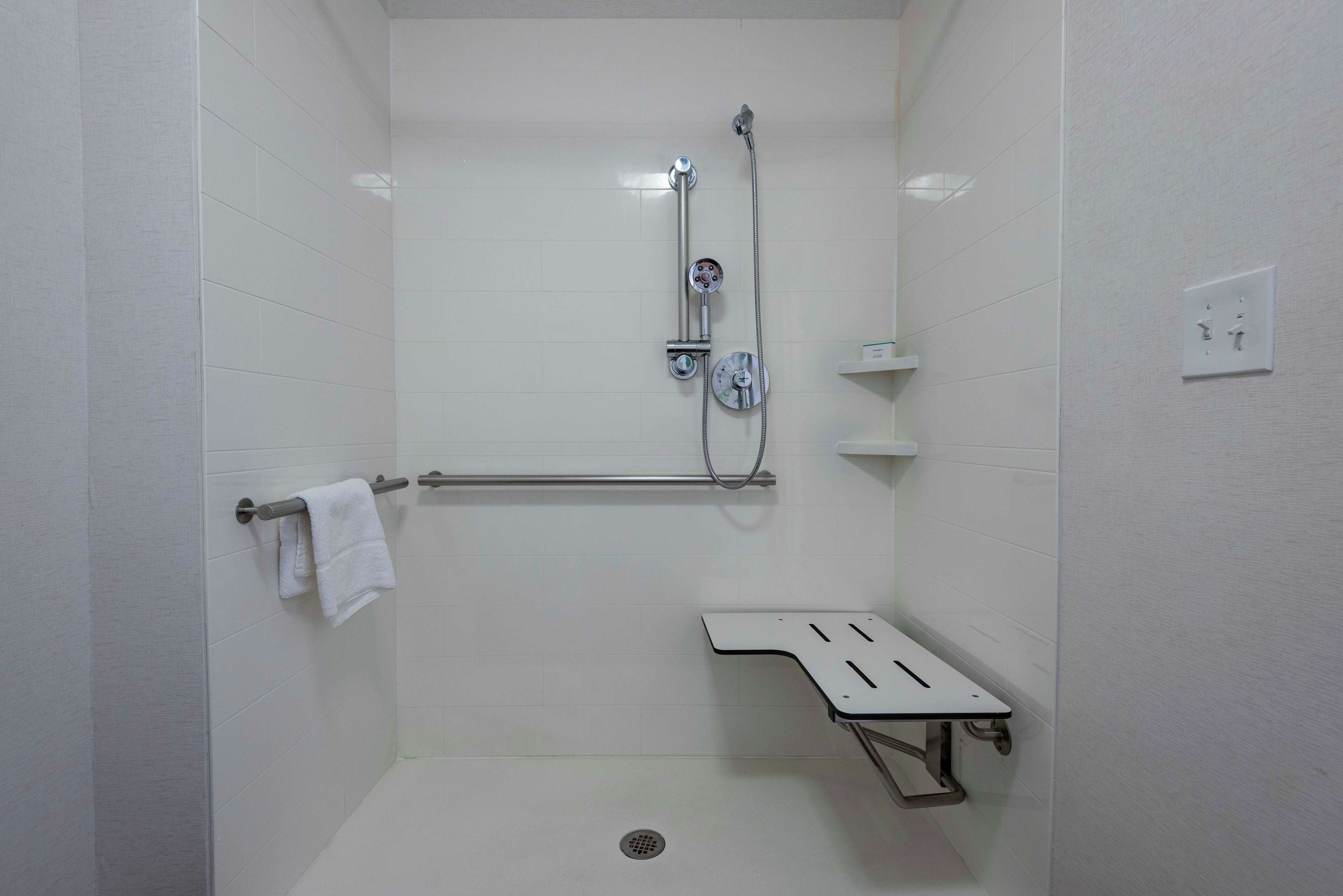Un espacio de ducha pequeño, con azulejos blancos, un cabezal de ducha de mano, un perchero y un estante pequeño.