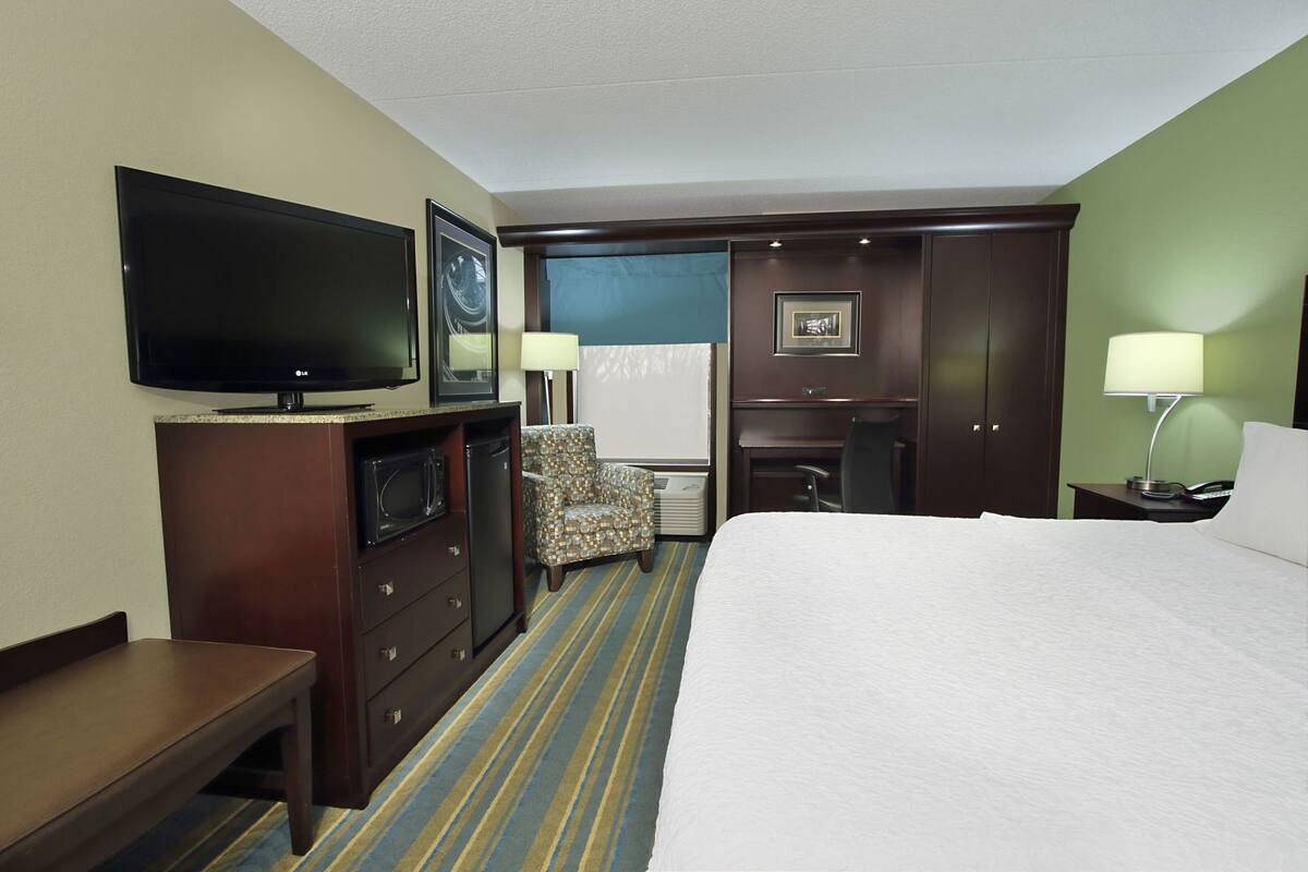 Habitación de hotel con cama, televisión, escritorio, silla y una pequeña cocina.