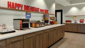 A breakfast area with a sign that reads "HAPPY BREAKFAST STARTS HERE." It includes a bakery section, a coffee station, and various food items on the counter. - Hampton Inn Hagerstown (Hagerstown)
