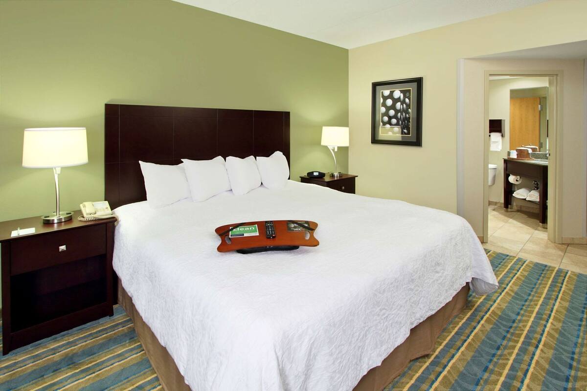 Habitación de hotel con una cama grande, dos mesitas de noche con lámparas, un teléfono en la mesita y un control remoto, además de un cuadro en la pared.
