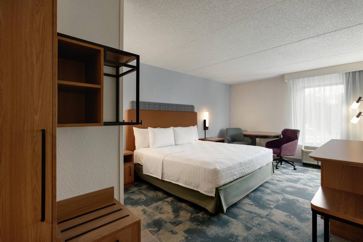 Una habitación de hotel con una cama grande, un escritorio, una silla, un armario y una ventana con cortinas.