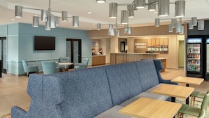 A modern interior with a seating area featuring a blue sofa and wooden tables, a bar area, and a beverage machine. - Hampton Inn Hagerstown (Hagerstown)