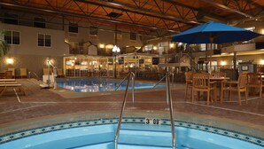 Una piscina interior amb un videt blau, una indicació de profunditat de 3 peus i 9 polzades, i cadires i taules de fusta al voltant de la zona de la piscina.