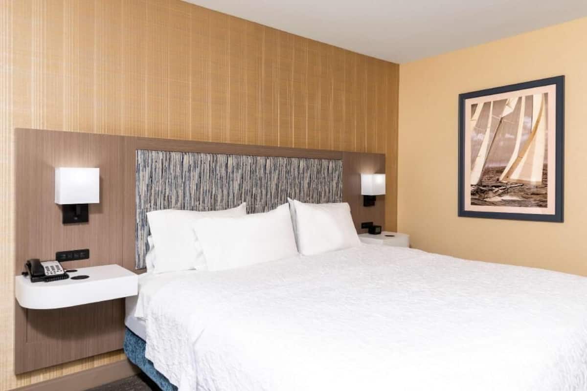 A hotel room with a large bed, bedside tables with lamps, a phone, and a framed picture on the wall.