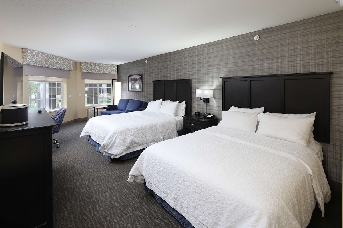 A hotel room with two beds, a desk, a chair, and a window.