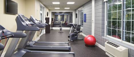 Een sportschool met loopbanden, hometrainers en een rode fitnessbal.