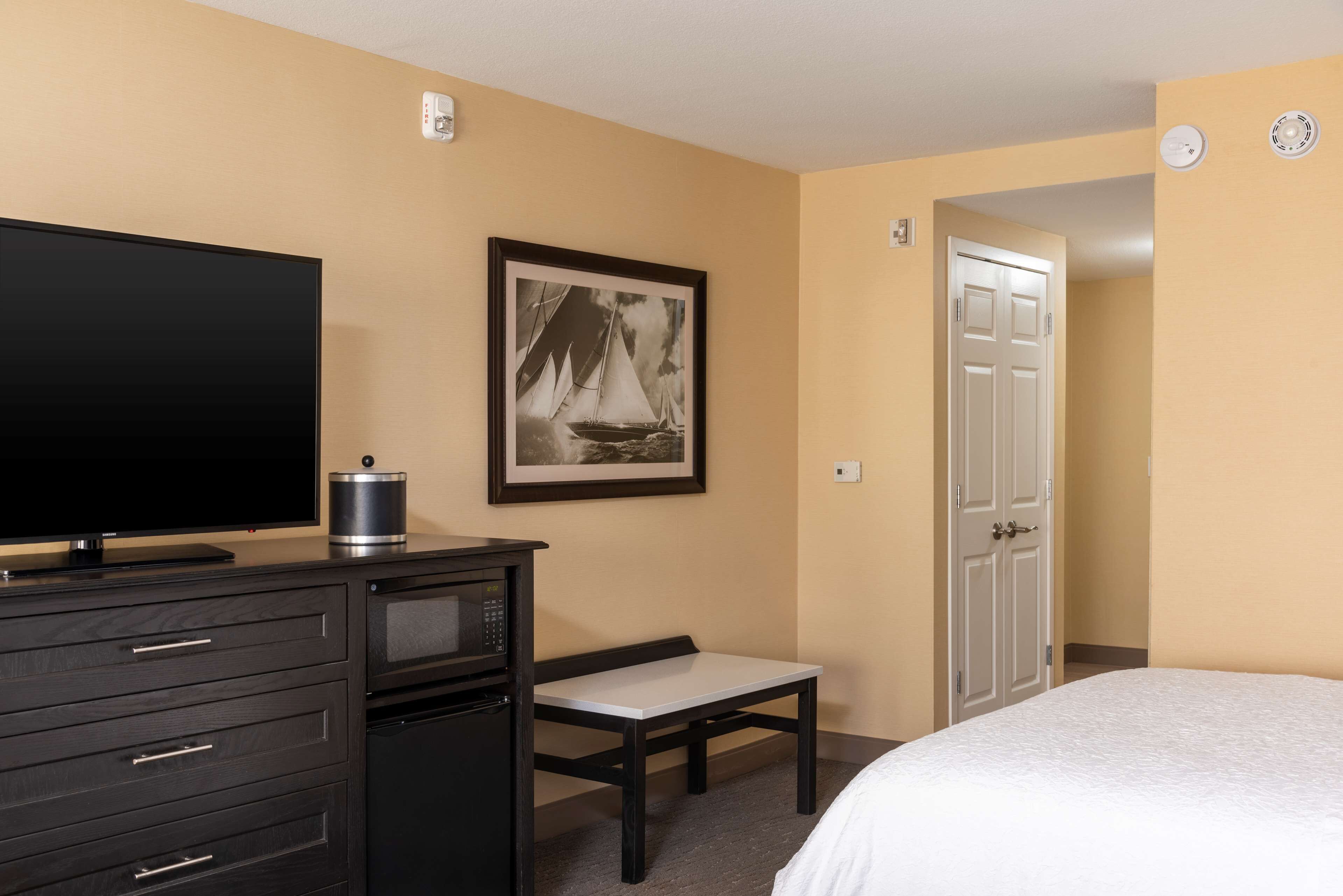 Une chambre d’hôtel avec un lit, une télévision, un bureau avec une chaise, un tableau encadré au mur et une porte.