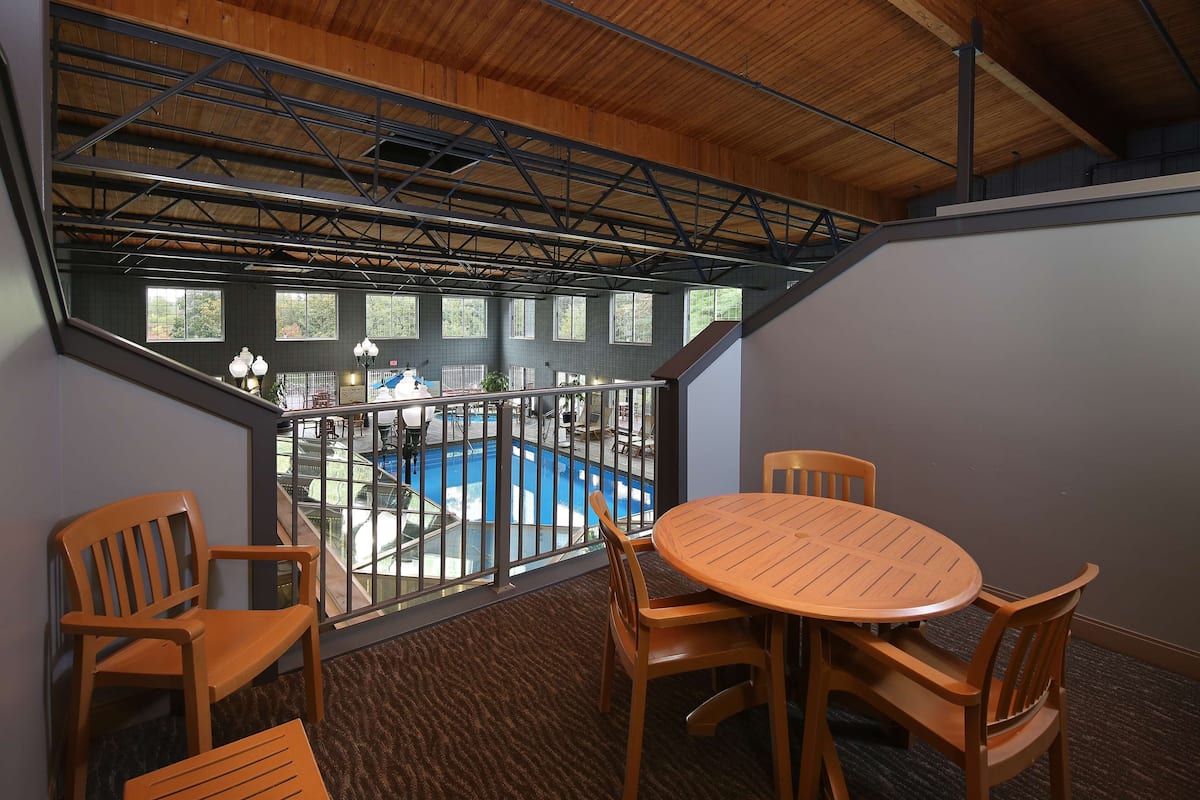 A balcony with a pool view, wooden furniture, and a high ceiling with metal beams.
