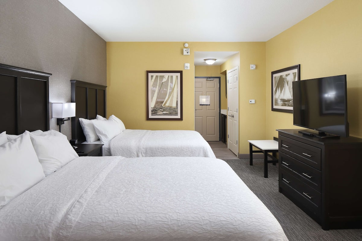 A hotel room with two beds, a dresser, a TV, and artwork on the walls.