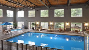 An indoor swimming pool with tiled walls, large windows, and poolside seating.