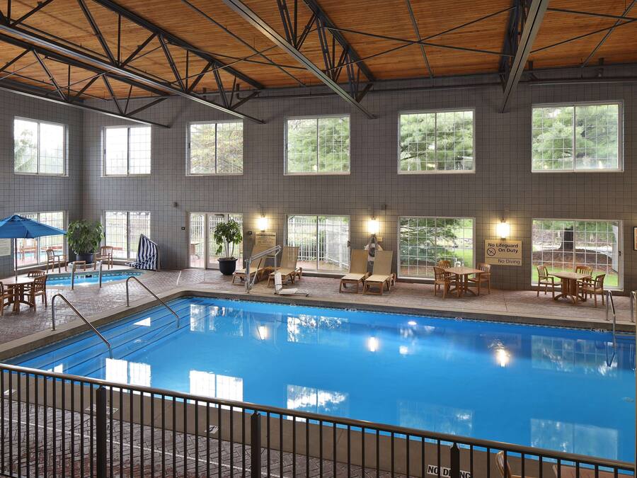 An indoor swimming pool with tiled walls, large windows, and poolside seating.