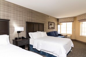 A hotel room with a large bed, a bedside table with a lamp, a chair, and a window with curtains.