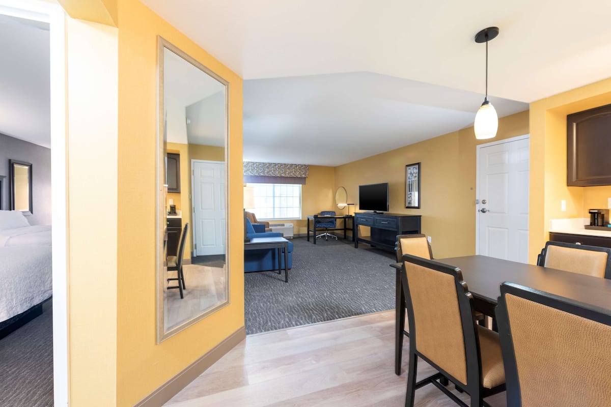 A hotel room with a bed, a desk, a chair, a TV, and a dining table with chairs.