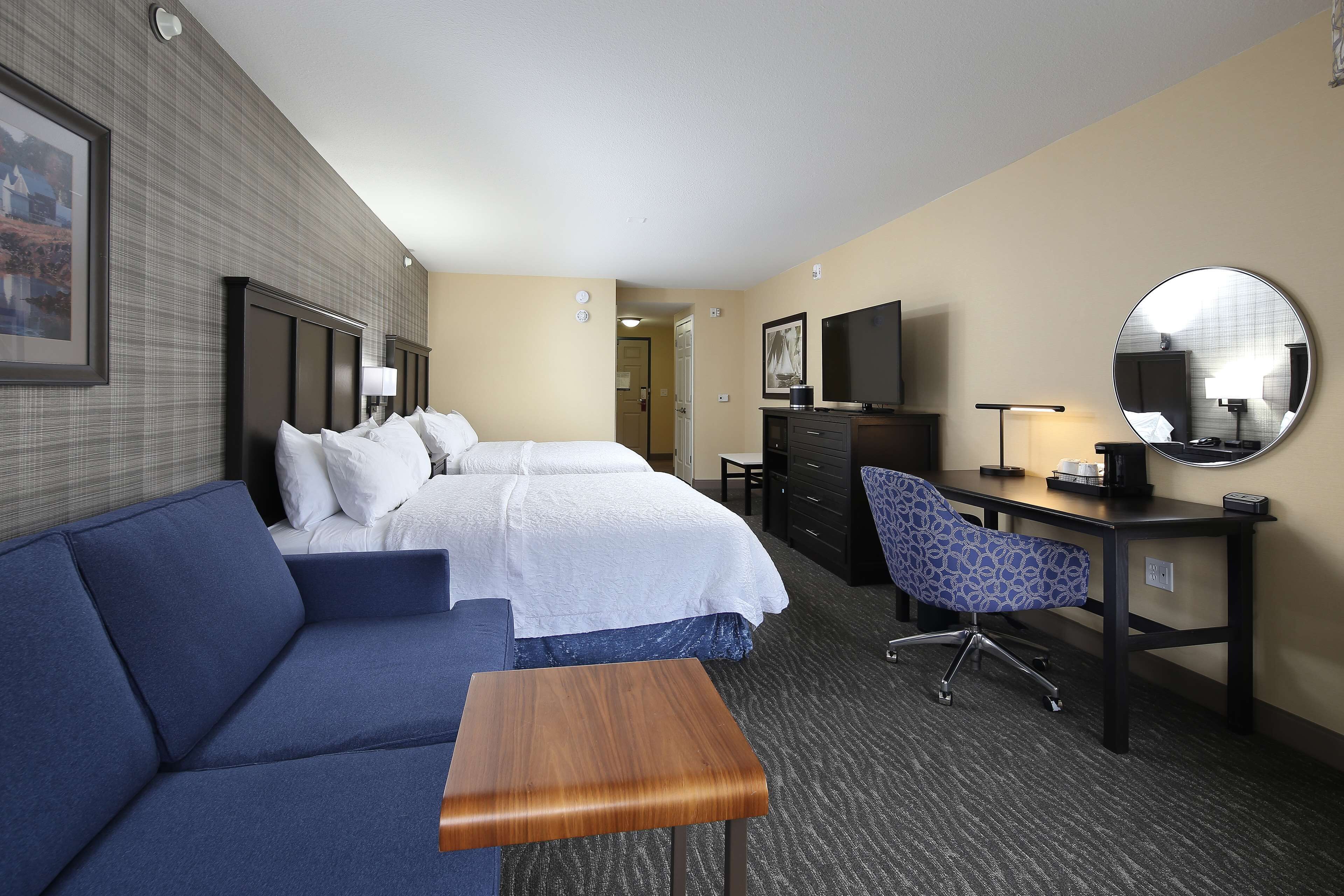 A hotel room with a large bed, a sofa, a desk with a chair, a TV, and a mirror.