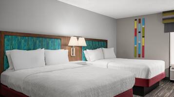 A hotel room with two beds, a wooden headboard, a wall-mounted lamp, and a colorful abstract art piece.