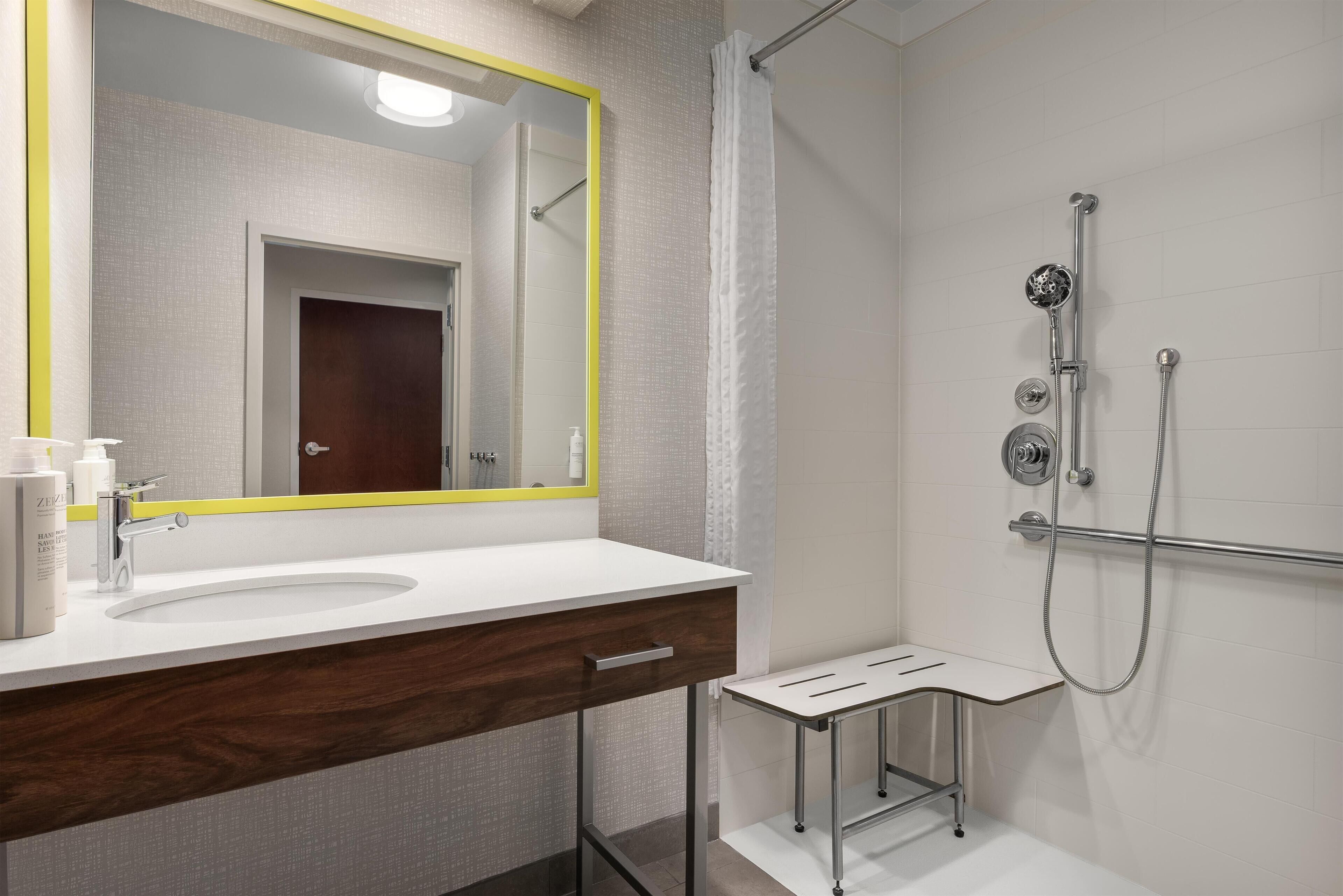 A modern bathroom with a white sink, a mirror with a yellow frame, and a shower area with a handheld showerhead.