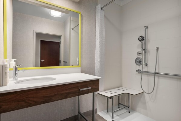 A modern bathroom with a white sink, a mirror with a yellow frame, and a shower area with a handheld showerhead.