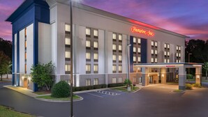 A modern hotel with a prominent "Hampton Inn" sign, a well-lit entrance, and a parking lot.