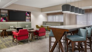 A modern lounge area with a sofa, red chairs, a bar area, and a flat-screen TV.