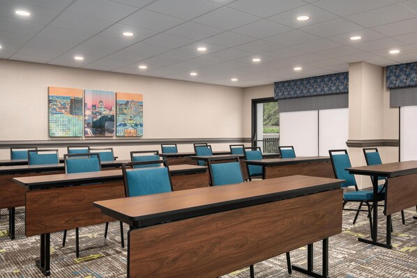 A conference room with multiple tables and chairs, a large window with a view, and a cityscape painting on the wall.