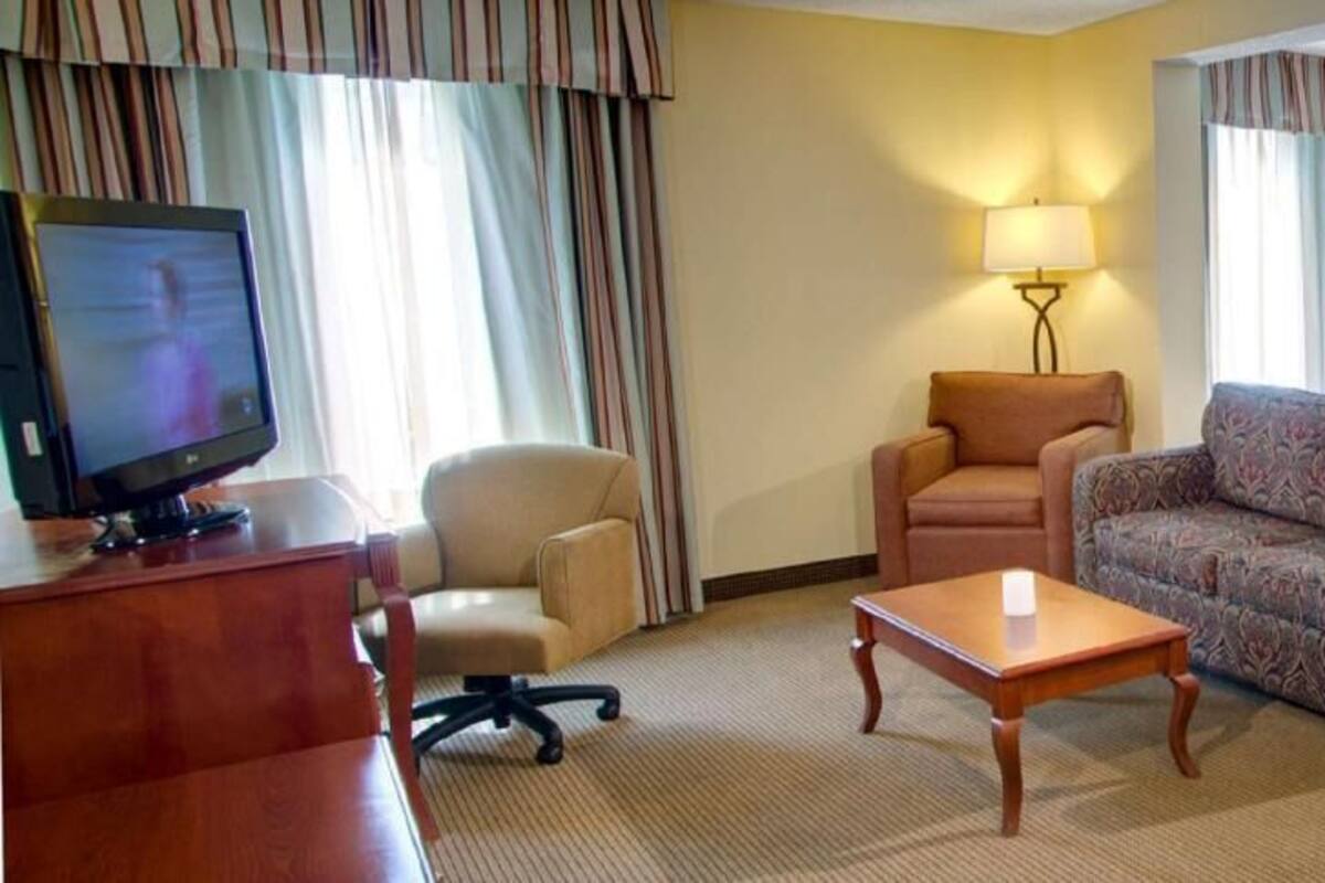A hotel room with a television, a desk, a sofa, a bed, and two lamps.