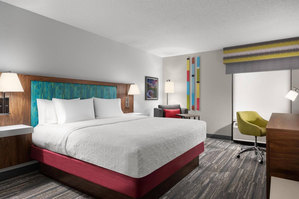 A hotel room with a large bed, a desk, a chair, and a lamp.