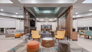 A modern lobby with a central seating area featuring round ottomans and chairs, a patterned rug, and a glass partition wall. - La Quinta Inn & Suites by Wyndham Sherman (Sherman)