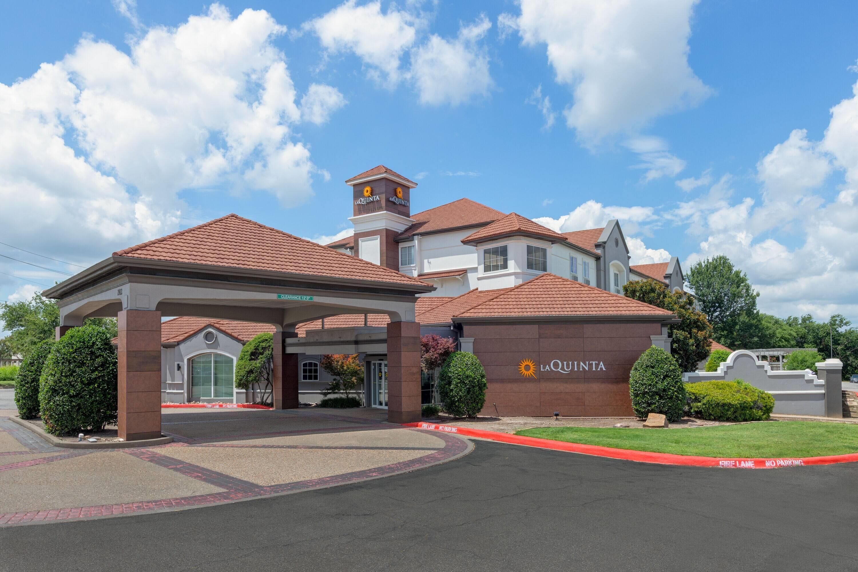 A hotel entrance with a covered driveway, a parking area, and a clear sky.