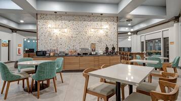 A modern dining area with round tables and chairs, a kitchen counter, and a decorative wall with a speckled pattern.