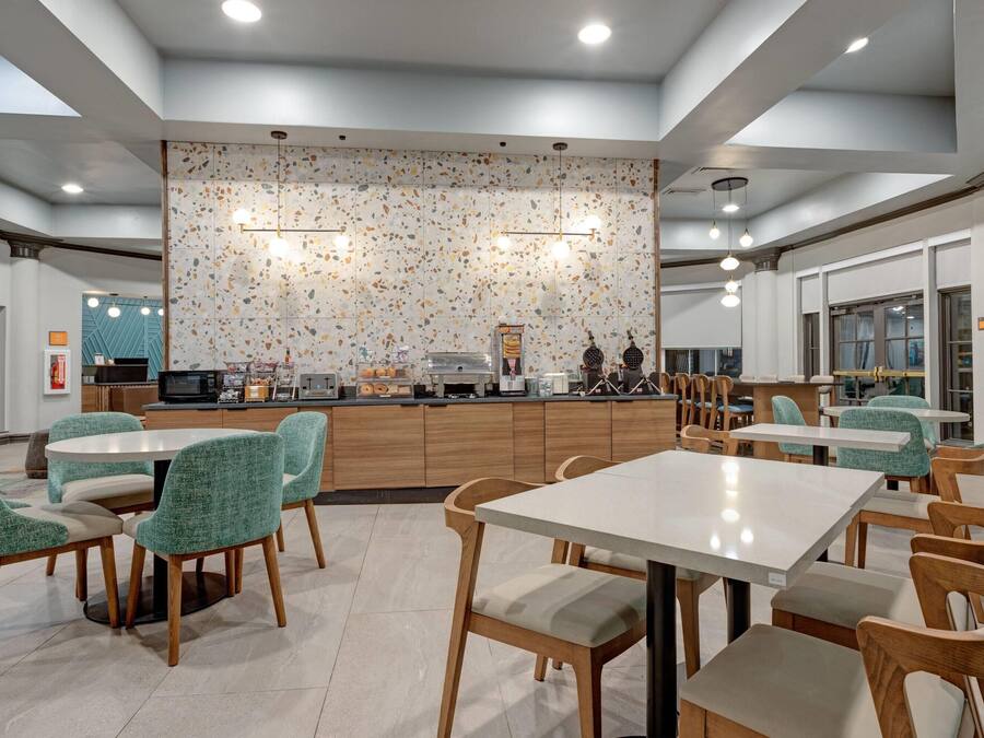 A modern dining area with round tables and chairs, a kitchen counter, and a decorative wall with a speckled pattern.