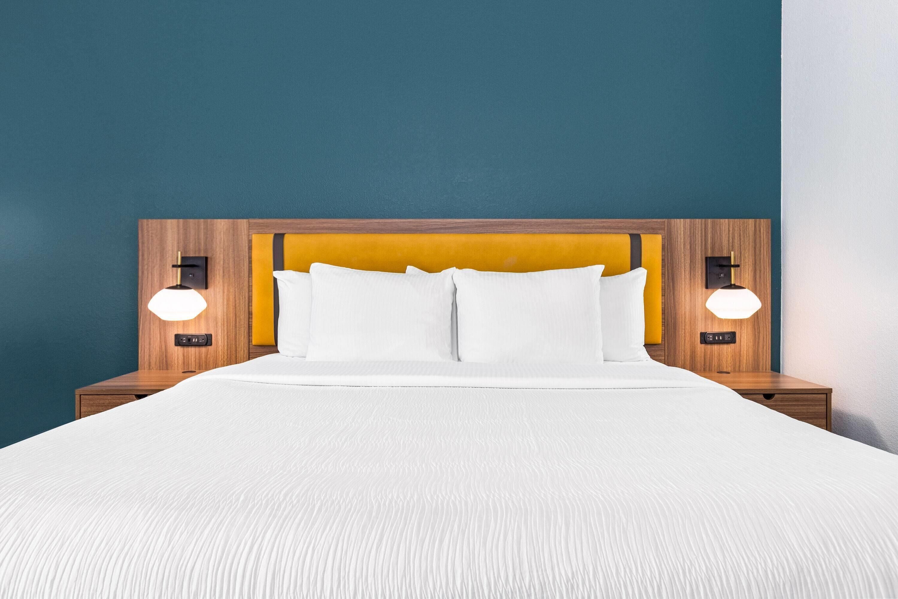 A neatly made bed with white linens and a wooden headboard. There are two bedside tables with lamps on either side of the bed.