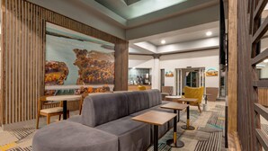 A modern interior with a grey sofa, wooden tables, and a large mural depicting a landscape. - La Quinta Inn & Suites by Wyndham Sherman (Sherman)