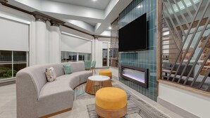 A modern living room with a sectional sofa, ottomans, a flat-screen TV, and a fireplace. - La Quinta Inn & Suites by Wyndham Sherman (Sherman)