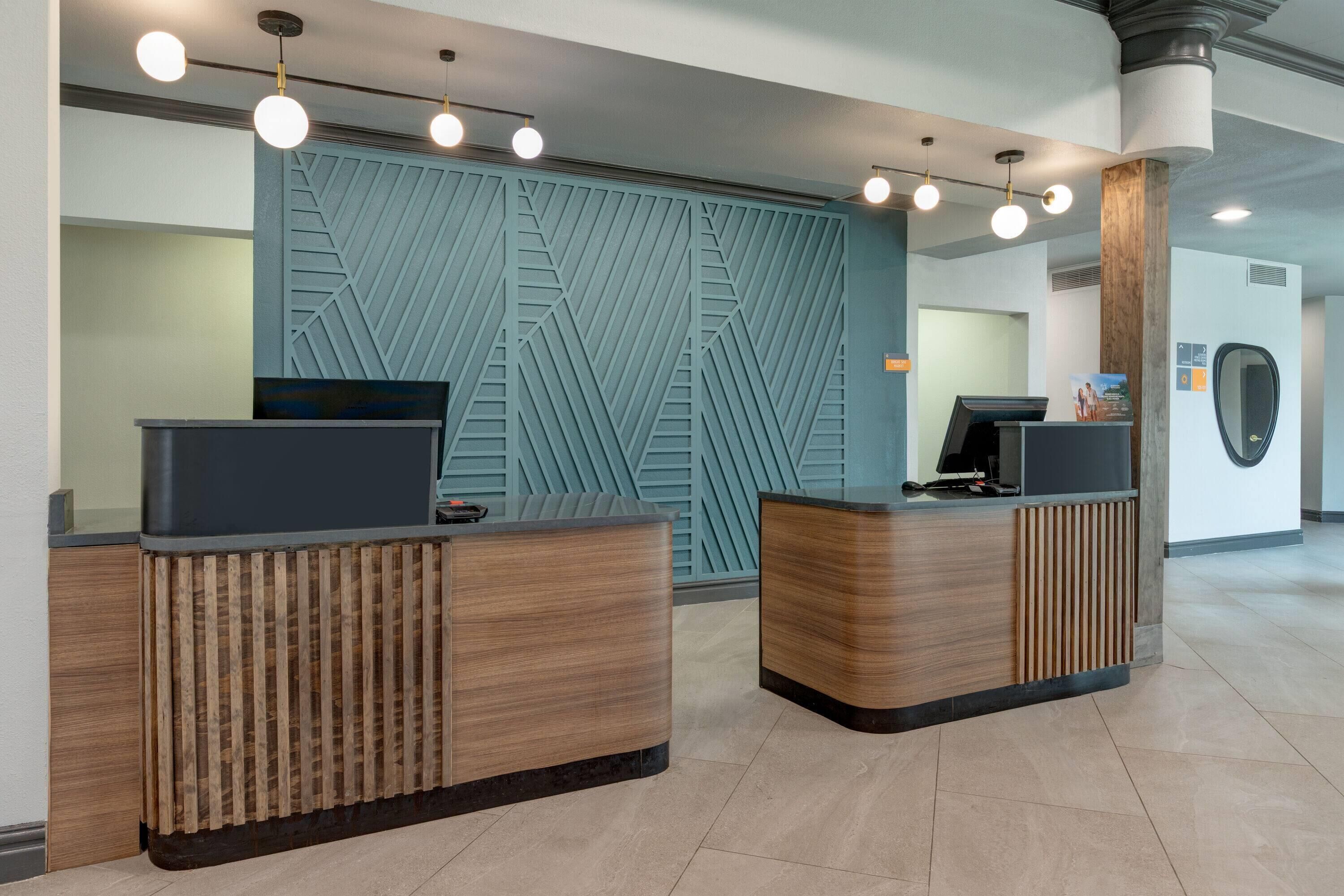 Un área de recepción con dos mostradores de madera, una pared azul con diseño geométrico y un espejo redondo a la derecha.
