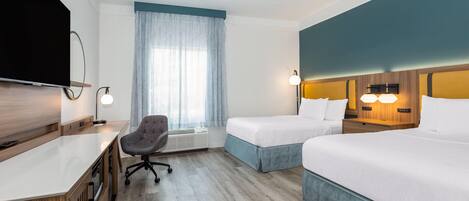 A hotel room with a desk, two beds, a TV, a chair, and a window with curtains.