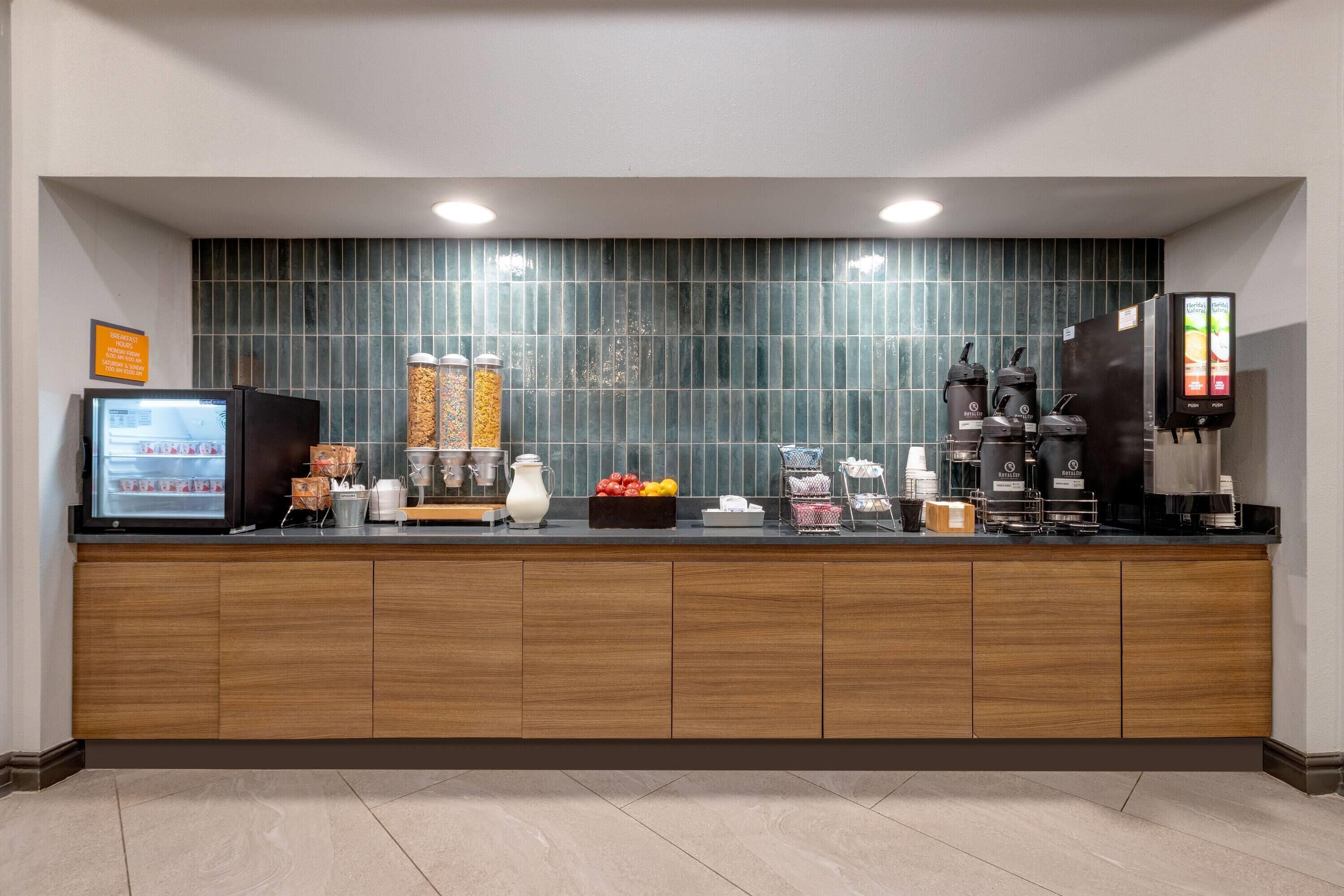 Zona de recepción de un hotel moderno con mostrador de madera, refrigerador, máquinas de café y un revoque de azulejos.