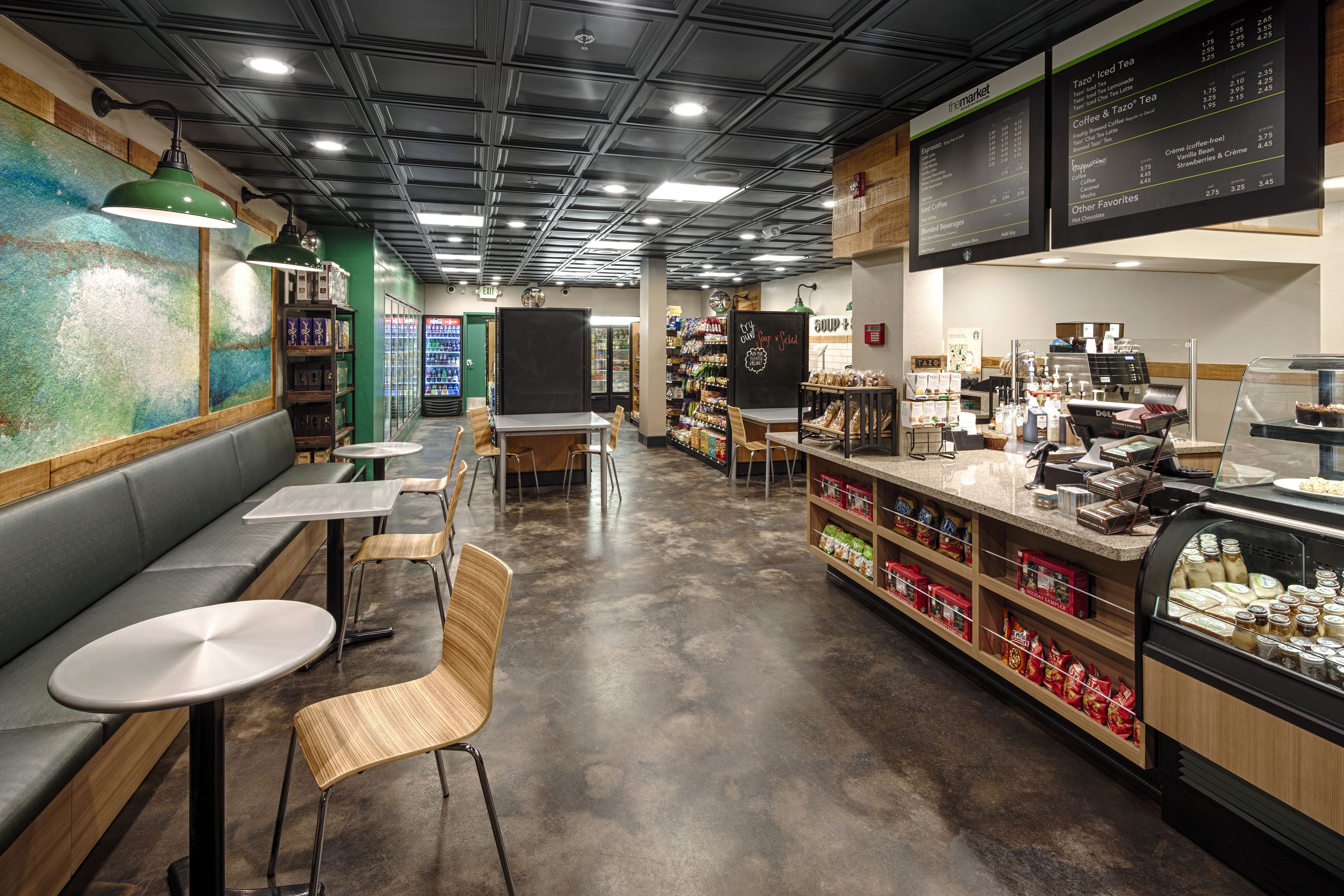 Una cafetería con mesas, un mostrador con productos alimenticios y una pizarra de menú.